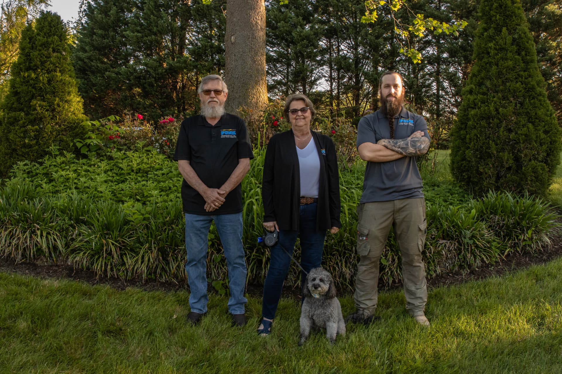 Funk Electrical owners Lin, Danny, and Eric standing outdoors with the office dog